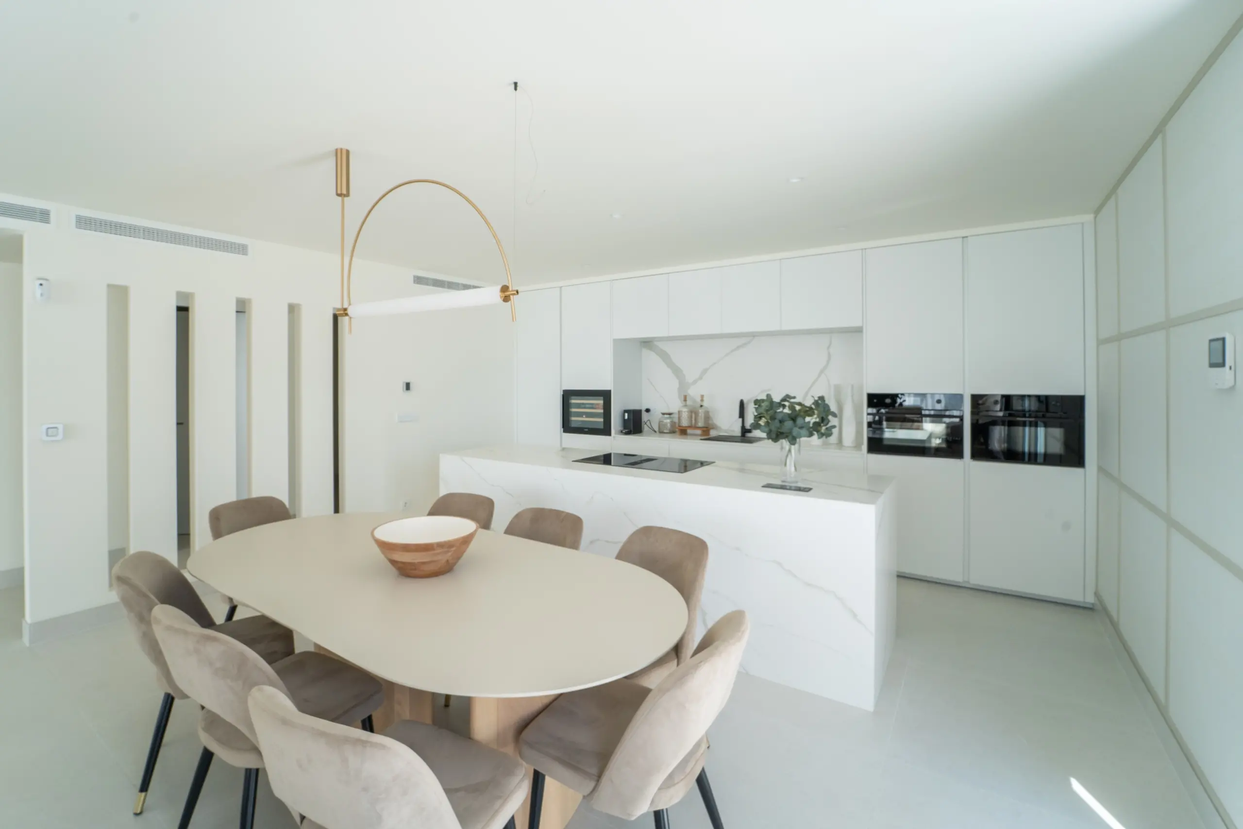Amplia cocina con una isla central que funciona también como comedor, equipada con electrodomésticos modernos y gabinetes blancos. Sobre la isla, una lámpara colgante de estilo moderno añade un toque de elegancia. El espacio es luminoso y acogedor con tonos claros.
